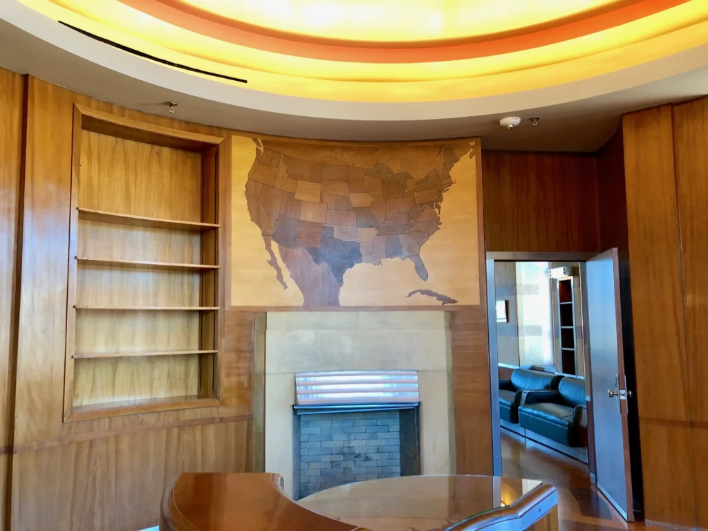 Art Deco executive office with wood-paneled curved walls, a built-in bookcase, a fireplace and a wooden map
