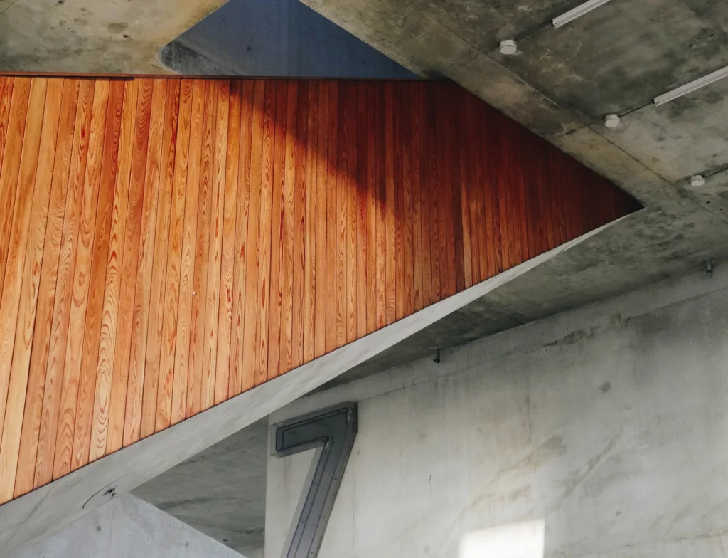 Warm-toned wood-clad stair surface beside bare concrete ceiling and walls