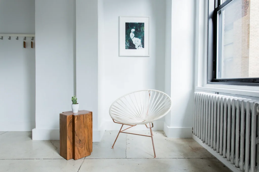 Une chaise seule et une table d'appoint en bois massif dans un coin blanc baigné par la lumière d'une fenêtre